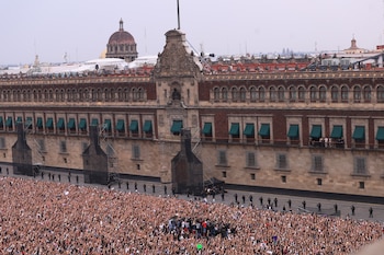 Vista aérea de una multitud de personas con los brazos en alto frente al Palacio Nacional; algunas personas y personal de seguridad se ven en un balcón del edificio