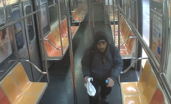 Interior de un vagón de metro con asientos naranjas y amarillos. Un hombre con chaqueta, capucha y mochila camina por el pasillo