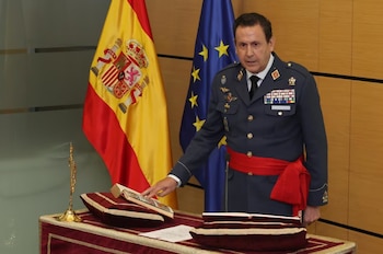 Militar de uniforme con fajín rojo apoya la mano sobre un libro abierto ante las banderas de España y la Unión Europea junto a un crucifijo
