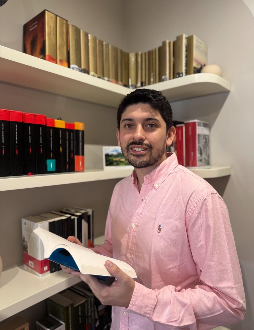 El escritor peruano Diego Nieves sostiene un libro junto a una estantería durante la presentación de su novela Reos de colores.