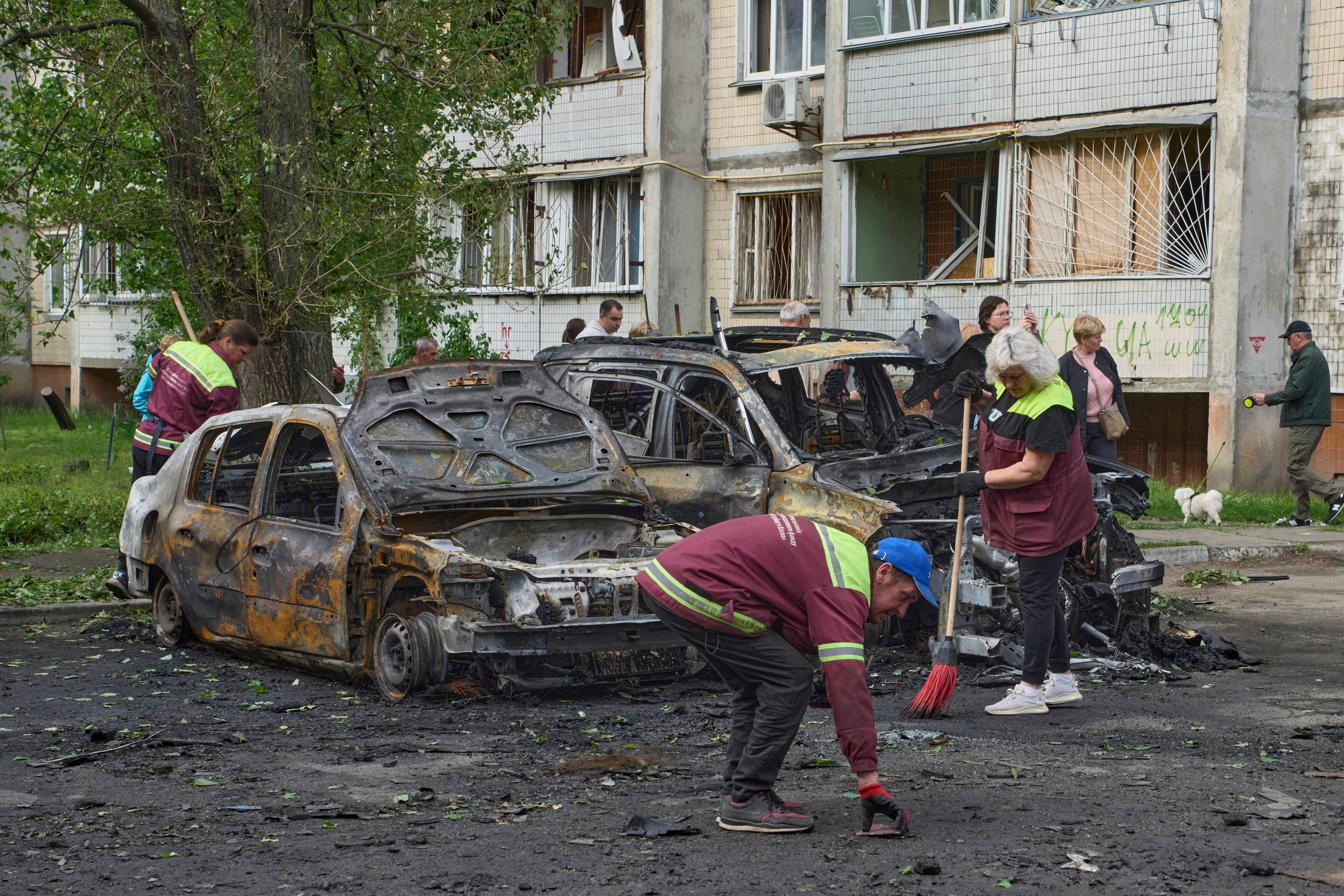 Trabajadores municipales limpian escombros en torno a autos quemados en la zona residencial tras los drones de ataque en Kiev, Ucrania, el domingo 4 de mayo de 2025. (AP Foto/Efrem Lukatsky)