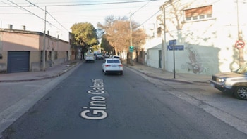 Vista urbana a nivel de calle con el nombre Gino Galeotti escrito sobre el pavimento, flanqueada por casas, árboles y automóviles