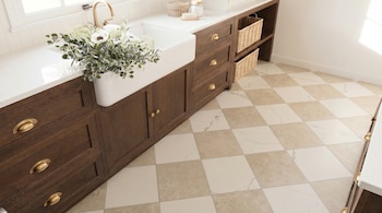 Vista aérea de una moderna cocina con piso de baldosas a cuadros beige y blanco. Se ven gabinetes de madera oscura, un fregadero blanco, un grifo dorado y un jarrón de flores.