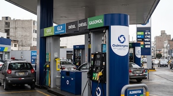 Surtidores de combustible con cartelera de precios y el logotipo de Osinergmin en una estación de servicio con vehículos estacionados.