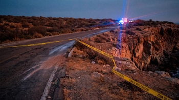Cinta amarilla de investigación policial en una carretera de asfalto cerca de un acantilado, con luces rojas y azules a lo lejos.