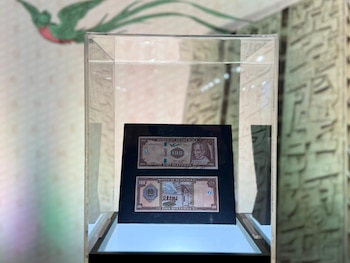 Dos billetes de 100 Quetzales de Guatemala, uno mostrando el anverso y otro el reverso, dentro de una vitrina transparente