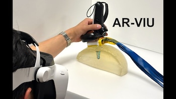 Persona con gafas de realidad virtual sostiene un transductor de ultrasonido sobre un modelo transparente con una estructura digital 3D visible. Se lee AR-VIU