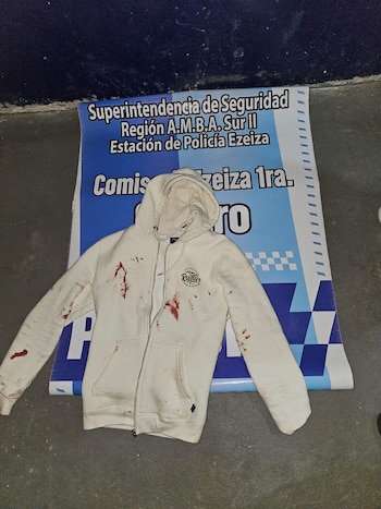 Una campera blanca con capucha y manchas de sangre sobre un cartel impreso de la policía en el suelo