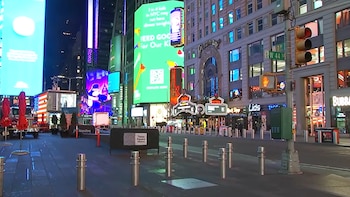 Vista nocturna de Times Square en Nueva York, con grandes pantallas luminosas, edificios, un semáforo rojo y la calle 44