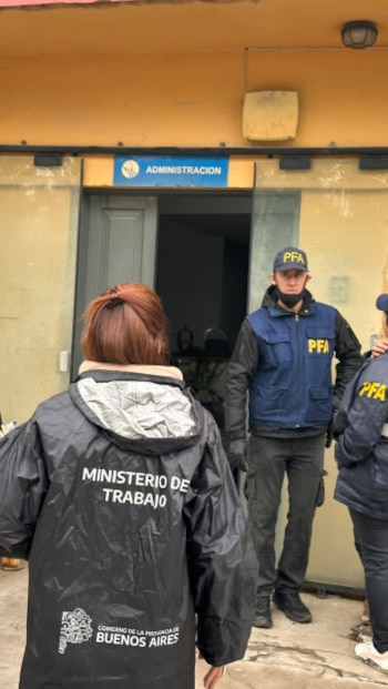 Un agente de la Policía Federal Argentina y personal del Ministerio de Trabajo bonaerense frente a una puerta con el cartel Administración