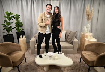 Nicolás Magaldi y Pampita sonríen de pie frente a un sofá en un estudio con cortinas claras, plantas, una mesa de centro baja y dos sillones individuales