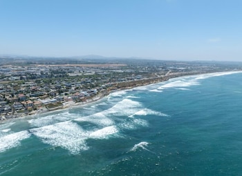 Vista aérea de una costa con edificios, una playa, acantilados de arena y el océano con olas bajo un cielo despejado