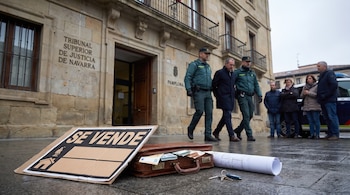 Dos agentes escoltan a un hombre ante el Tribunal Superior de Justicia de Navarra junto a un cartel de venta, un maletín con dinero y unos planos.