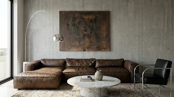 Salón moderno con sofá seccional de cuero marrón, mesa de centro de mármol, sillón negro, lámpara de arco y pintura abstracta en pared de hormigón.