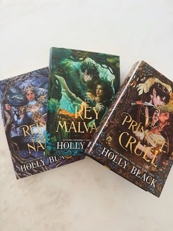 Tres libros con cubiertas ilustradas en tonos oscuros sobre una superficie blanca, con los títulos "El Rey Malvado", "La Reina Nada" y "El Príncipe Cruel" visibles