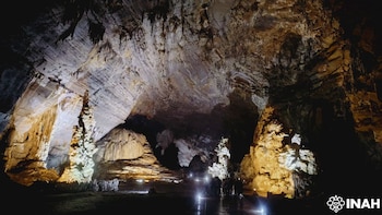 Caverna subterránea iluminada con estalactitas en el techo, grandes estalagmitas en el suelo, luces artificiales y siluetas de personas