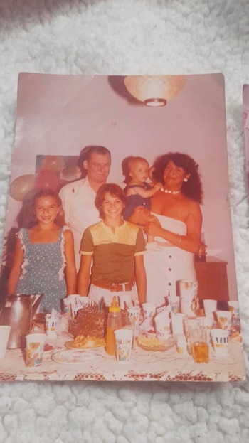 Fotografía impresa de dos adultos y tres niños detrás de una mesa con un pastel de cumpleaños, vasos, jarras y platos