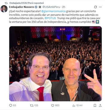 Foto de dos hombres sonrientes tomando una selfi frente a una multitud y un edificio iluminado de rojo y azul por la noche