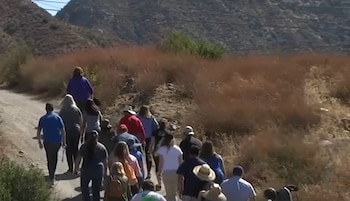 Un grupo de personas camina de espaldas por un camino de tierra entre vegetación seca y colinas