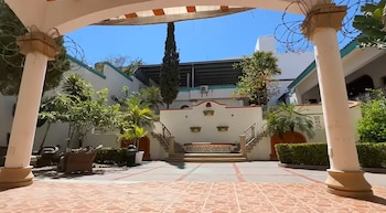 Patio con piso de baldosas, columnas en primer plano, escaleras centrales, palmeras y una pared decorada