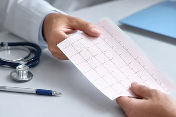Las manos de un médico y de un paciente sostienen una tira de electrocardiograma sobre un escritorio con estetoscopio y bolígrafo.