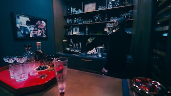 Persona bebiendo de una copa en un bar de diseño interior. Estantes con cristalería, decantadores, botellas, una bandeja con vasos y un cuadro