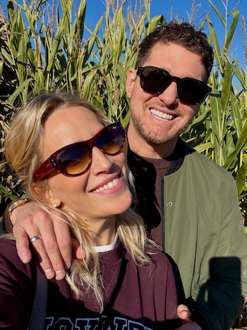 Una mujer y un hombre con gafas de sol sonríen juntos en primer plano delante de una plantación de maíz bajo la luz del sol