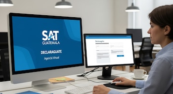 Vista lateral de una mujer usando dos computadoras. La pantalla izquierda muestra el logo de SAT Guatemala y la derecha un formulario de declaración.
