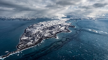 Vista aérea de una península montañosa cubierta de nieve rodeada por aguas oscuras con una grieta submarina visible a lo largo de la costa.