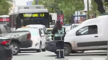 Un agente con uniforme y chaleco reflectante de espaldas en una calle con automóviles, furgonetas y un autobús
