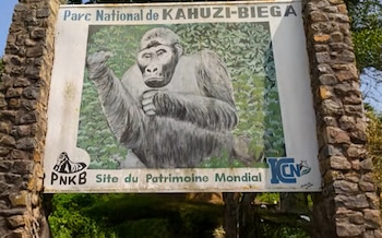 Cartel de bienvenida al Parque Nacional Kahuzi-Biega, sostenido por pilares de piedra, con una pintura de un gorila y texto en francés