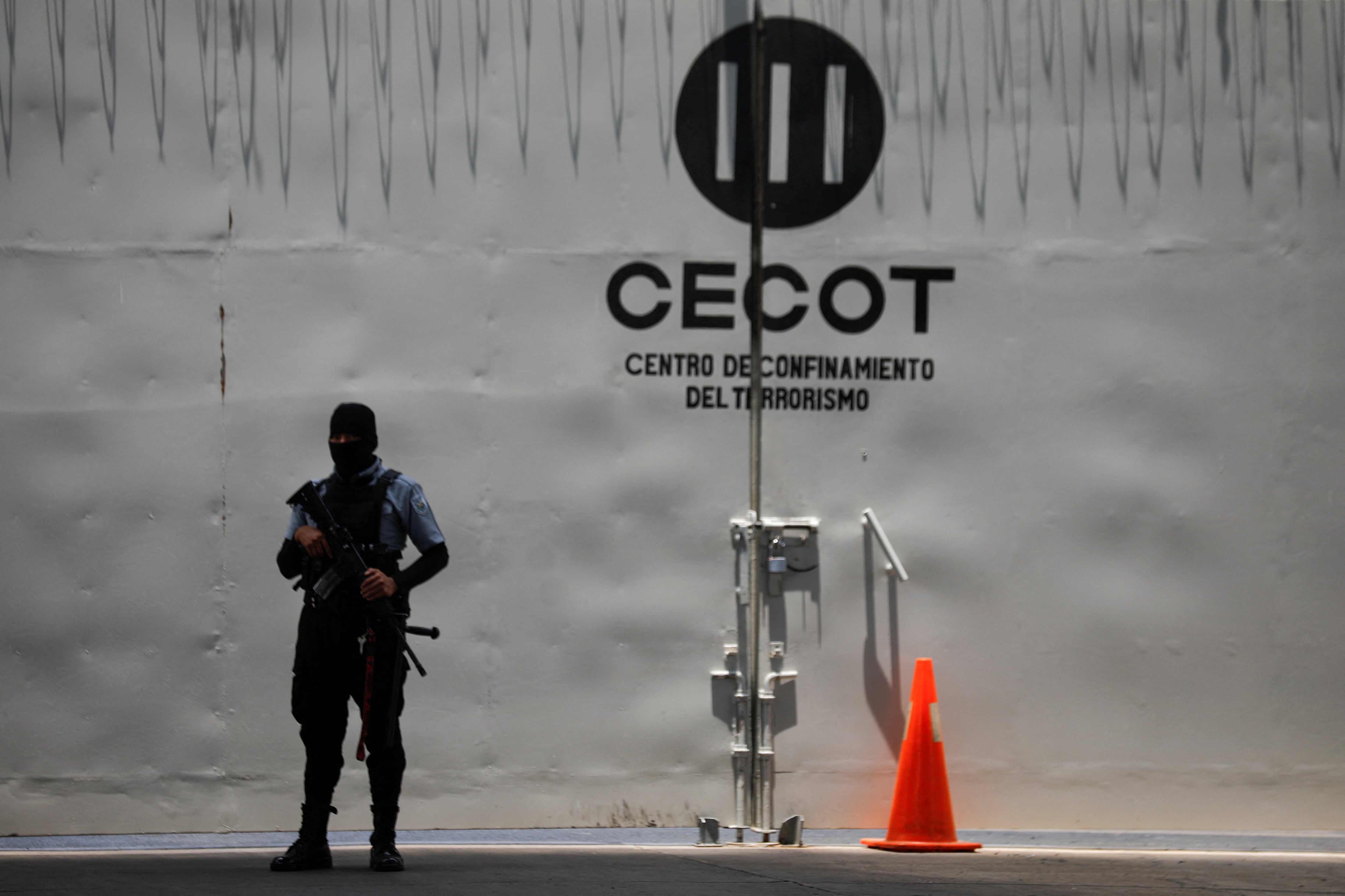 FOTO DE ARCHIVO: Un guardia penitenciario se encuentra cerca del logotipo del CECOT, mientras presuntos miembros de la banda Mara Salvatrucha, también conocida como MS-13, asisten a una audiencia pública en un juicio colectivo, después de que 486 presuntos miembros de la banda fueran acusados de más de 47.000 delitos cometidos entre 2012 y 2022, según la fiscalía, en el Centro de Confinamiento para Terroristas (CECOT) en Tecoluca, El Salvador, el 23 de abril de 2026. REUTERS/Jose Cabezas/Archivo