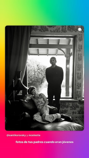 Fotografía en blanco y negro de una mujer sentada en un sofá y un hombre de pie junto a una ventana con árboles al fondo, dentro de una habitación