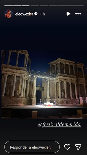 Vista nocturna de un teatro romano antiguo con columnas y edificios de piedra. Hay dos personas en el escenario con una mesa iluminada por focos