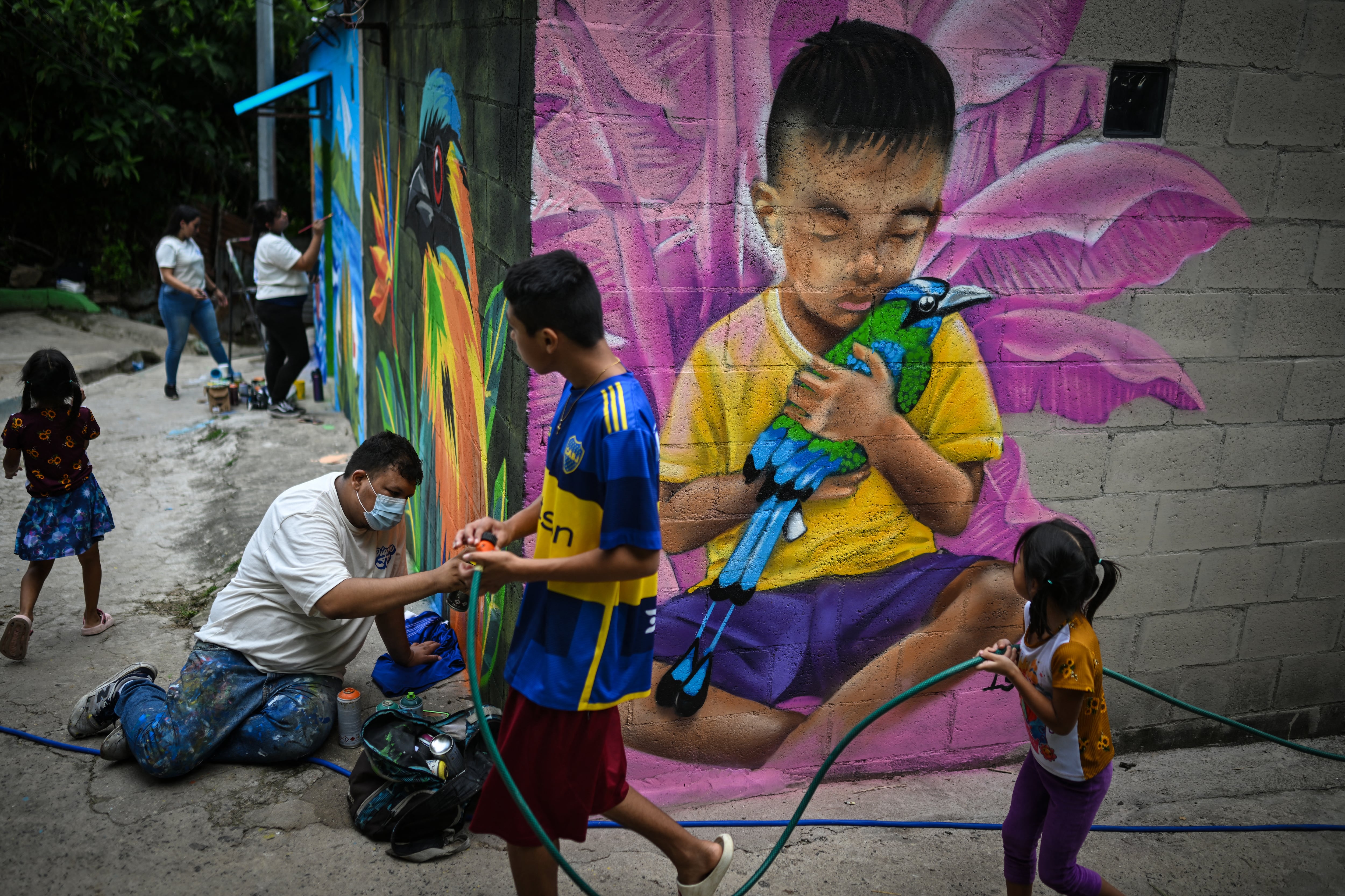 El artista salvadoreño Carlos Clímaco (izq.) pinta un mural junto a varias artistas femeninas en la comunidad 10 de Octubre de San Marcos, El Salvador, el 2 de octubre de 2026. El proyecto artístico busca transformar la identidad de una comunidad históricamente afectada por la violencia de las pandillas. (Foto de Marvin RECINOS / AFP)