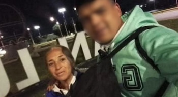 Una mujer y un joven con el rostro difuminado posan de noche frente a unas letras gigantes iluminadas en un espacio público
