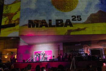 Cuatro músicos tocan en un escenario frente a un edificio iluminado con el texto MALBA 25