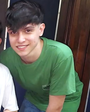 Primer plano de Agustín Rivero, un joven con cabello oscuro y sonrisa con frenillos, vistiendo una camiseta verde, posando frente a un fondo oscuro y de madera