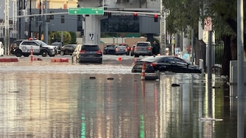 Una calle inundada con varios automóviles parcialmente cubiertos por agua, una patrulla policial y carteles de tráfico vial