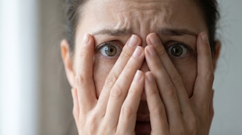 Primer plano del rostro de una mujer que se cubre los ojos con ambas manos, revelando solo sus ojos abiertos y parte de su frente arrugada entre los dedos.