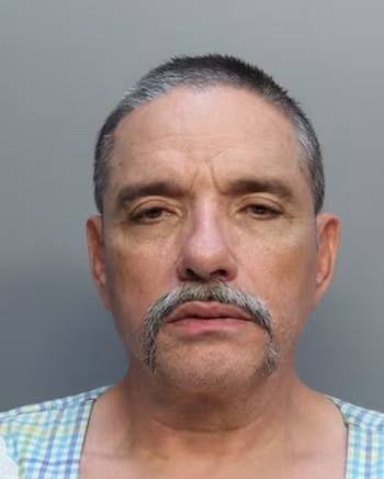 Retrato policial de un hombre adulto con cabello corto canoso, bigote y camisa de cuadros sobre un fondo gris neutro