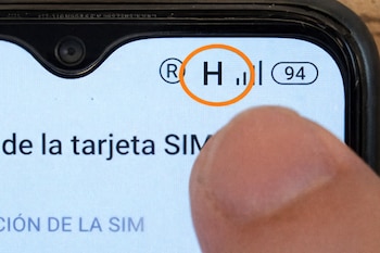 Primer plano de la pantalla de un celular que muestra un icono H en un círculo naranja, barras de señal, número 94, y parte de un dedo.