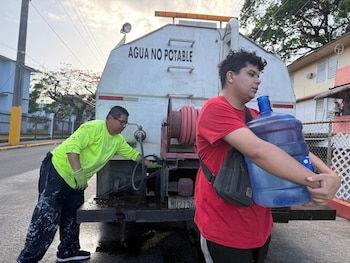 Bryan Pérez carga con una garrafa de agua para su departamento en el complejo de viviendas públicas Villa Kennedy, en San Juan, Puerto Rico, el 10 de junio de 2026. / AP Foto - Dánica Coto