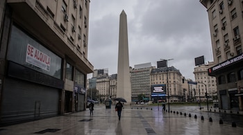 El Obelisco de Buenos Aires en un día lluvioso con peatones con paraguas, un local con cartel de alquiler y pantallas con texto.
