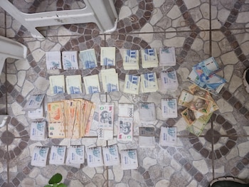 Vista aérea de billetes de pesos argentinos de 1000, 2000, 10000 y 20000, junto a otras monedas, esparcidos sobre un suelo de baldosas