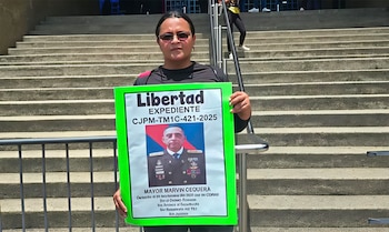 Una mujer ante unas escaleras de concreto sostiene un cartel verde con la foto de un militar y la palabra Libertad