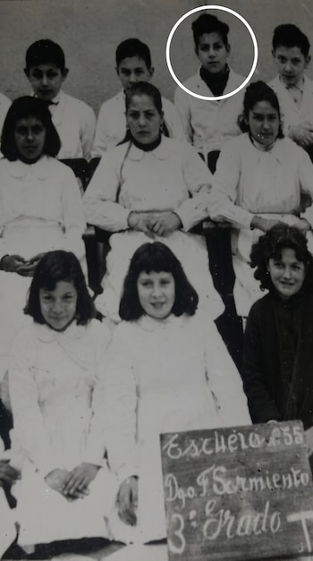 Fotografía en blanco y negro de once alumnos de tercer grado, dispuestos en tres filas, con un círculo blanco alrededor de un niño. Un cartel indica el nombre de la escuela.