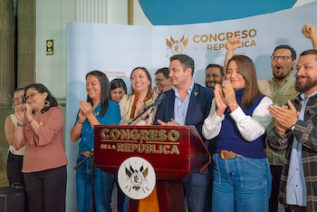 Grupo de personas, incluyendo un hombre en un podio con micrófono, aplaudiendo y sonriendo. Detrás, un panel blanco con el logo y el nombre "Congreso de la República"