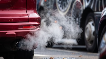 Parte trasera de un automóvil de color rojo que emite humo blanco a través del tubo de escape.