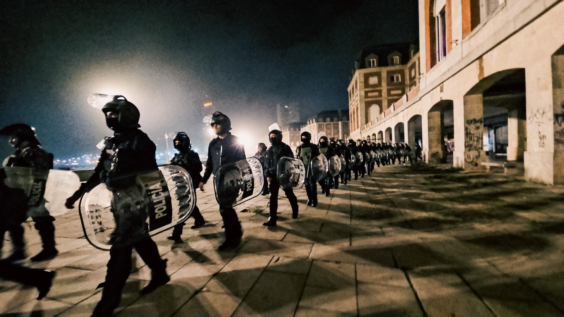 Una fila de agentes de policía antidisturbios equipados con cascos y escudos marcha para proceder con el operativo